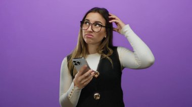Gözlük takan genç bir kadın, mor arka plana karşı akıllı telefon tutarken şaşırmış görünüyor. Teknolojik yanlış anlaşılma ya da kafa karışıklığı olduğunu gösteriyor.