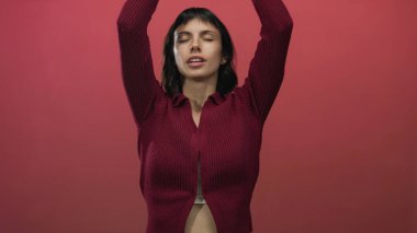 Kadın ellerini başının üstüne koyar ve kollarını kaldırır. Stüdyoda kırmızı duvara karşı göbeğini ortaya çıkarır. Huzur..