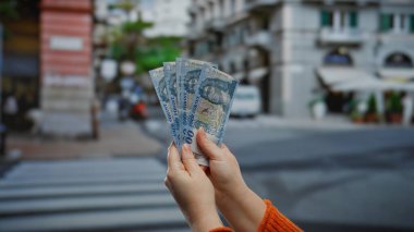 Kentsel şehir caddesinde elinde Macar banknotları tutan kadın açık havada iş ve para değişimi yapıyor, ekonomik işlemleri ve mali faaliyetleri vurguluyor.