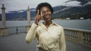 Kadın parmağıyla parmağıyla göl kenarındaki caddenin kenarını işaret ediyor, gülümsüyor, sevinç iyimserliği.