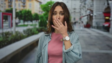 Şehir sokaklarında şaşkın bir ifadeyle genç bir İspanyol kadın, günlük kıyafetler giyiyor, şehir ortamında yüzünü ve duygularını vurguluyor..