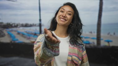Genç İspanyol kadın elini uzattı kumsalda kameraya gülümsüyordu; davet bağlantı sevinci.