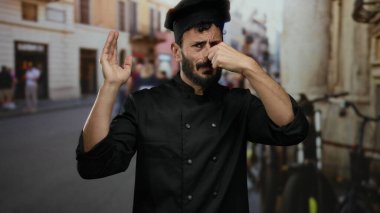 Siyah üniformalı İspanyol aşçı sokak ortamında burnunu çimdikliyor..