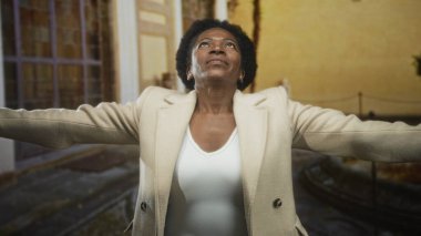 Beyaz bluzlu, kolları açık bir kadın binanın içine doğru bakıyor, umut verici bir esneklik..