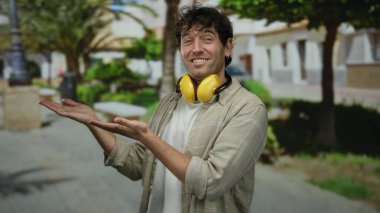 Cazibeli bir gülümsemesi olan, ses geçirmez kulaklıklar takan, güneşli bir sokakta ellerini uzatan, yemyeşil ve modern tarzlı bir şehir havası yakalayan İspanyol bir adam..