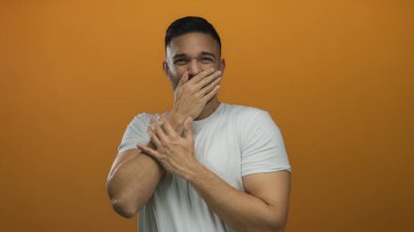 Parlak turuncu bir arkaplan karşısında duran genç bir adam sürpriz ya da kahkahaları canlı bir renk ve detayla yakaladığı sıradan bir ortamda ifade ediyor..