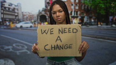 Yeşil gömlek ve örgülü karton protesto tabelası taşıyan kadın; sosyal değişim kararlılığı.