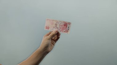 İzole edilmiş beyaz arka plan duvarına karşı elinde 10 lira banknot tutan adam, para ve finansmanı vurguluyor..
