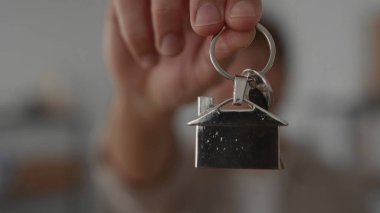 Gülümseyen adam ev anahtarlığını tutuyor, sıcak bir ev ortamında yeni ev sahipliğini sembolize ediyor.