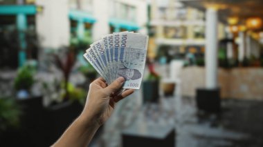 Hand holding south korean won banknotes in an outdoor city street setting, highlighting the concept of finance and commerce with a male presence.