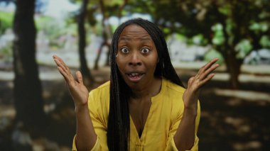 Güneşli bir parkta, açık sarı bir bluz giyen, yemyeşil ağaçlarla çevrili, açık havada neşeli bir anı yakalayan bir kadın..