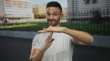 Genç adam şehrin sokaklarında gülümseyen beyaz gömlekli güneş ışığı altında jest yapıyor.