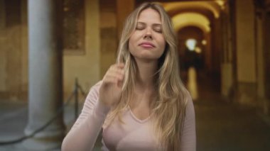 Sarışın, beyaz bir kadın üniversitede manastır kemerinde iki eliyle saç çekiyor..