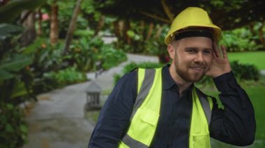 Sert şapkalı ve yansıtıcı yelekli bir adam ormanda kulaklarına yakın elle başparmak kaldırıyor. Güven, takım çalışması..