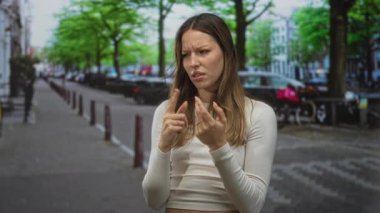 Kadın parmağı kaldırılmış elleri ve gergin ifadesiyle, şaşı kaşlarıyla ve büzüşmüş dudaklarıyla şehir caddesinde bir tarafı işaret ediyor..