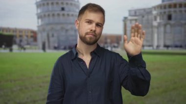 Adam sidik kulesinin önünde el sallıyor, avuç içi kameraya yükseliyor; dostça selamlaşma.