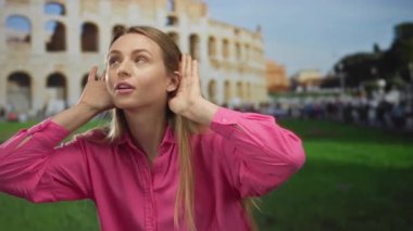 Roma sembolik kolezyumunun önünde el pençe divan duran genç bir kadın, açık hava kentsel ortamında merakını ve bağlılığını gösteriyor..