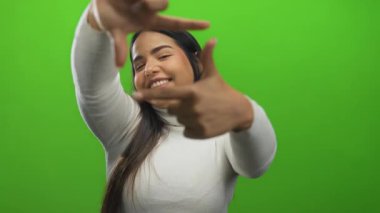 Çekim yapan kadın el ele tutuşurken gülümsüyor canlı yeşil arka planda yaratıcılık sergiliyor ve coşkulu ve oyuncu tavrıyla odaklanıyor..