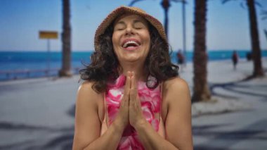 Yazın güneşli bir sahil geçidinde eğlenen bir kadın, çiçek kolyesi ve plaj şapkası takıyor, neşeli bir tatil ruhunun ruhunu yakalıyor..