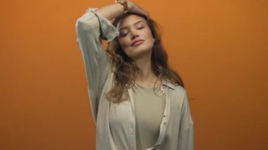 Uzun kahverengi saçlarını tarayan ve izole edilmiş turuncu bir stüdyo duvarına gülümseyen genç İspanyol kadın. Kendine güvenen zarif kadın..