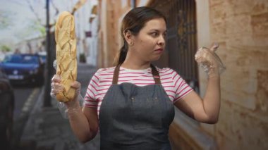 Eldivenli eldiveni olan bir kadın bir binanın ön cephesinde bir caddede baget tutuyor; kayıtsızlık rutini.