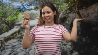 Bir orman yolunda sol el ve sağ avuç içi ile kek tutan bir kadın gülümsüyor; neşeli atıştırmalık an paylaşmak.