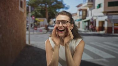 Dürbünlü ve ağaçlı bir caddedeki yaya geçidinde elleri ağıza sokulmuş bir kadın arıyor..