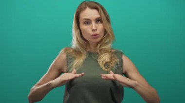 Sarı saçlı bir kadın derin derin nefes alır, yeşil bir arka planda izole edilmiş, sakin ve rahatlamış görünüyor, ve yeşil kolsuz bir üst giyiyor..