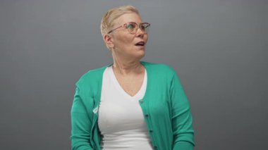 Gri stüdyoda açık ağızlı, gözlüklü, yeşil hırkalı ve beyaz yakalı bir kadın..