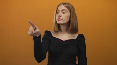 Turuncu arkaplan üzerine odaklanan, izole edilmiş bir ortamda siyah giysili bir kadın. Yön ve duyguyu görsel olarak modern tarzda çekici kılıyor..