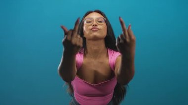 Stüdyoda orta parmakları açık, pembe bluz ve gözlük takan bir kadın..