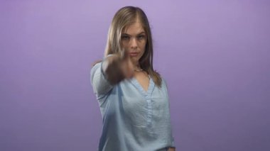 Açık mavi gömlekli kadın, mor stüdyo alanına odaklanmış bakışlarıyla doğrudan kamerayı işaret ediyor..