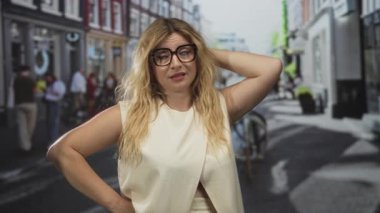 Meşgul caddede kafaya ve kalça üstüne dokunan gözlüklü genç sarışın kadın dükkanlarla dolu..