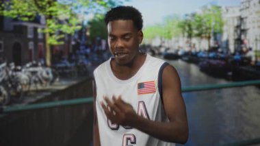 ABD basketbol forması giyen bir adam City Street Köprüsü 'nde kanal kenarında göğsü işaret ediyor..