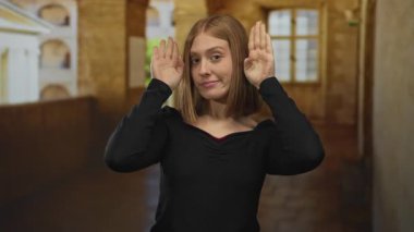 Arka planda pencereleri ve kemerleri olan eski bir kasaba caddesinde el hareketlerini ifade eden genç sarışın bir kadını gösteren bir kadın..