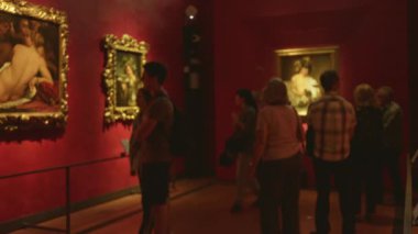 Sığ bokeh ve sıcak kırmızı duvarlar, çerçevelenmiş resimler ve yumuşatılmış ışıklandırma ile bulanık müze içi; arka plan şablonu.