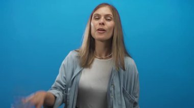Parlak mavi bir stüdyoda jest yapan, dili dışarı çıkmış kot gömlek giyen genç sarışın kadın, şakacı..