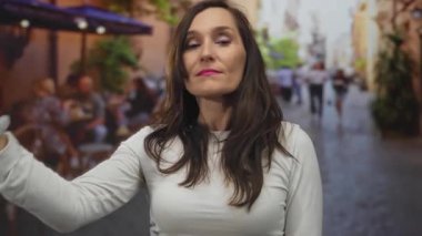 Şehir hayatı ile çevrili kalabalık bir sokak terasında, açık bir restoranda güven içinde el kol hareketi yapan bir kadın..