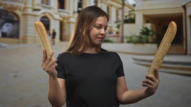 Süslü bir binanın önündeki bir caddede her iki elinde de iki baget tutan bir kadın. Kararsızlık..