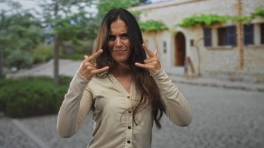 Taş bir binanın yanındaki kaldırım taşı bir sokakta iki eliyle taş el hareketi yapan bir kadın..