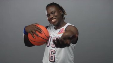 Mavi bileklikli turuncu basketbol topu tutan ve elini gri stüdyoda uzatan bir adam; neşe takımı gururu.