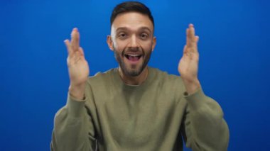 Elleri mavi bir arkaplan üzerinde gülümseyen genç bir adam, mutluluk ve açıklık kavramları için ideal, anlamlı bir jest olarak sevinç ve pozitifliği iletiyor..