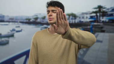 Bir adam gözlerini uzatır ve rıhtımdaki suyun kenarında genç bir İspanyol adamın yanında manzarayı kapatır..