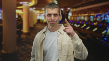 Kumar makineleriyle çevrili, canlı bir kumarhanede güvenle duran bir adam, hareketli kumar sahnesiyle meşgul olurken, sıradan ama odaklanmış bir tavır sergiliyor..