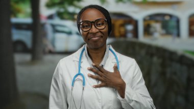 Sokakta steteskoplu gözlüklü, göğsünde gözlüklerle gülümseyen şehir manzaralı bir kadın..