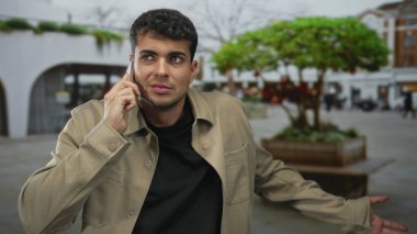 Akıllı telefonu kulağına dayayan ve şehir meydanında saçını okşayan bir adam. Öfke stresi..