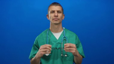 Yeşil üniformalı beyaz erkek doktor, steteskopu izole edilmiş mavi arka plana göre ayarlıyor..