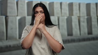 Şehir caddesinde dışarıda duran kadın endişeli ve duygusal görünüyor. Beton arka planda, anksiyete ve iç gözlem duygularını somutlaştırıyor..