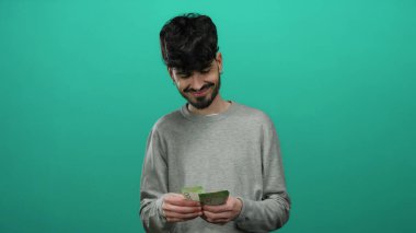 Elinde Rus rublesi banknotlar tutan bir adam izole edilmiş yeşil duvarlara gülümsüyor. Gri kazaklı..