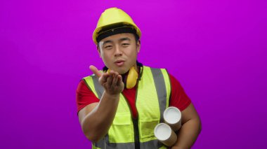 İnşaat malzemesi giyen Asyalı genç bir adam, elinde parlak pembe bir arkaplan planı tutarken öpüşüyor. Oyuncu ama profesyonel bir mimari tema sergiliyor..